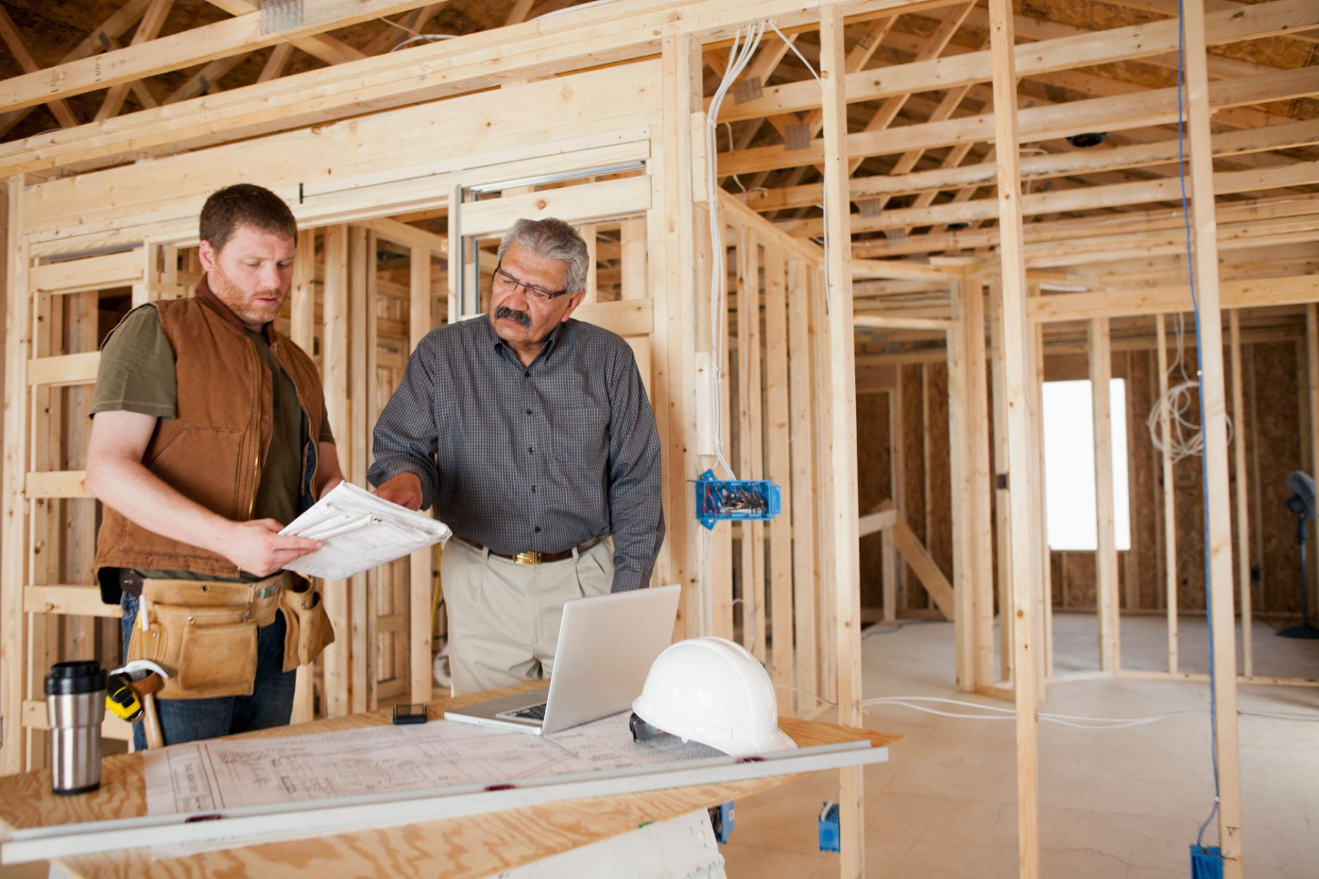 Contractor and builder reviewing plans inside a framed home